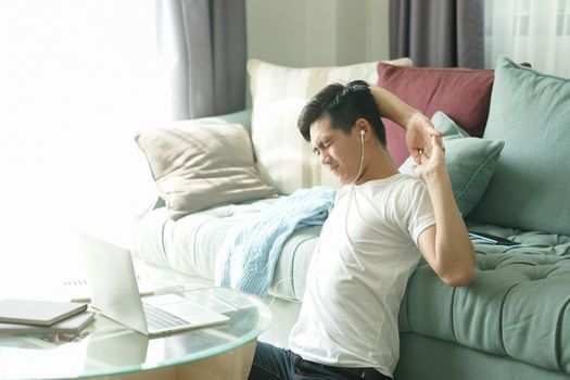asian young student man teenager entrepreneur wear earphones stretching feeling tired bored sleepy while working with computer studying learning online at home. e-learning education