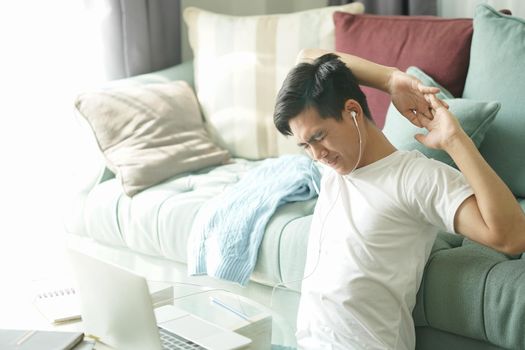 asian young student man teenager entrepreneur wear earphones stretching feeling tired bored sleepy while working with computer studying learning online at home. e-learning education