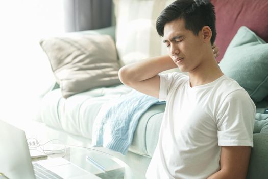 tired exhausted frustrated asian young student man teenager entrepreneur suffering from neck pain while working at home