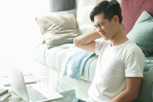 tired exhausted frustrated asian young student man teenager entrepreneur suffering from neck pain while working at home