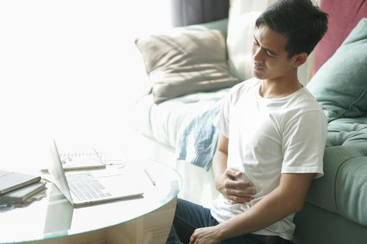 tired exhausted frustrated asian young student man teenager entrepreneur suffering from stomachache while working at home