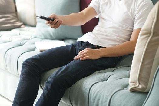 asian young teenage man pressing TV remote button on sofa at home