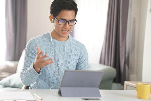 asian young teenage student man entrepreneur wear earphones working by video call conference studying learning online at home. e-learning webinar meeting. social distance in covid pandemic