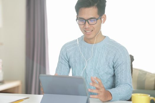 asian young teenage student man entrepreneur wear earphones working by video call conference studying learning online at home. e-learning webinar meeting. social distance in covid pandemic