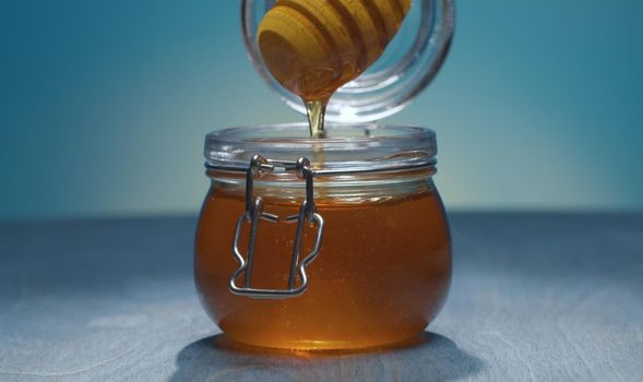 Close up honey pouring from honey spoon into a jar on blue background. Healthy fresh food concept