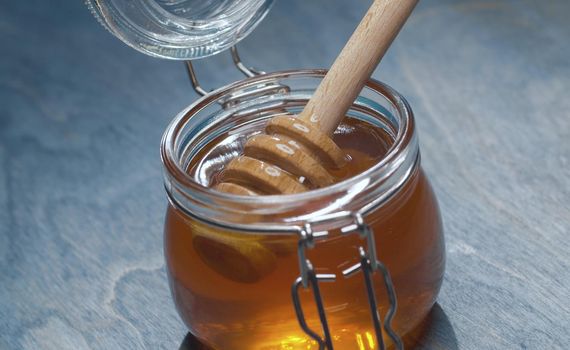 Close up fresh honey in glass jar on blue background. Healthy fresh food concept. High angle view