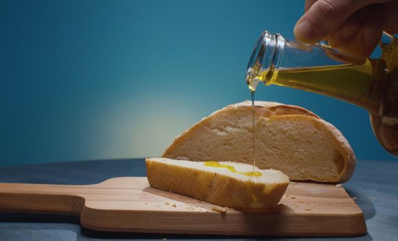 Close up male hand pouring olive oil on the piece of bread. Blue background. Healthy fresh food concept