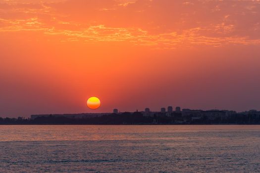 bright sunset over a calm sea and colorful sky with clouds at the background of the city