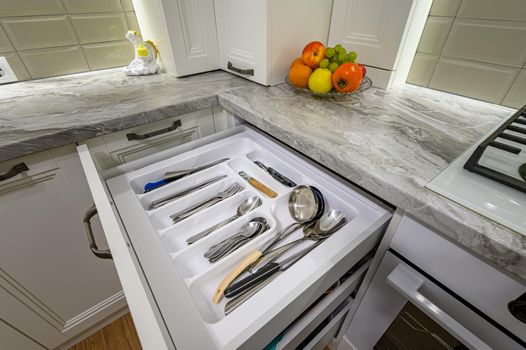 Closeup view to open drawers at white modern classic kitchen interior with wooden furniture, some drawers are open