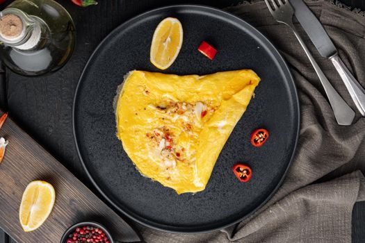 Spanish omelette, fresh red chilli, brown and white crabmeat, lemon, Cheddar cheese, eggs fried, on plate, on black wooden table background, top view flat lay