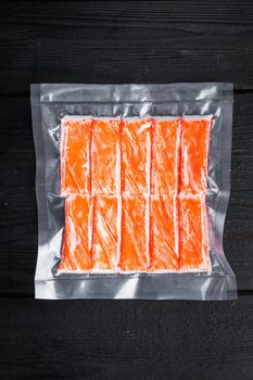 Crab sticks in vacuum pack set, on black wooden table background, top view flat lay
