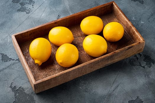 Fresh lemons set, in wooden box, on gray background