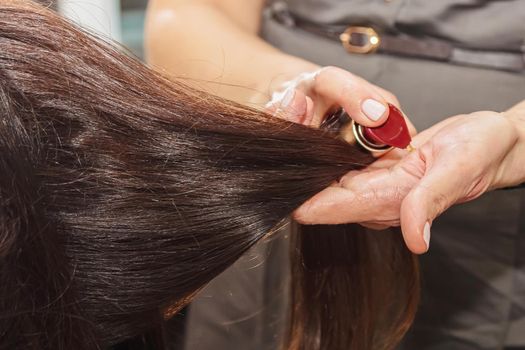 The hairdresser treats her hair by applying a nourishing agent to the girl's long hair.