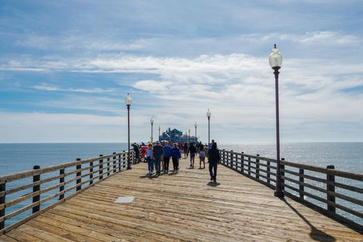 Tourist walking on the Oceanside Pier during blue summer day, Oceanside, northern San Diego, California. Wooden pier on the western United States coastline. Famous for fisher. Febraury 22n, 2020