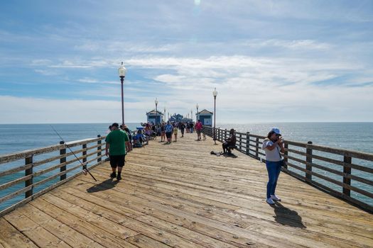 Tourist walking on the Oceanside Pier during blue summer day, Oceanside, northern San Diego, California. Wooden pier on the western United States coastline. Famous for fisher. Febraury 22n, 2020