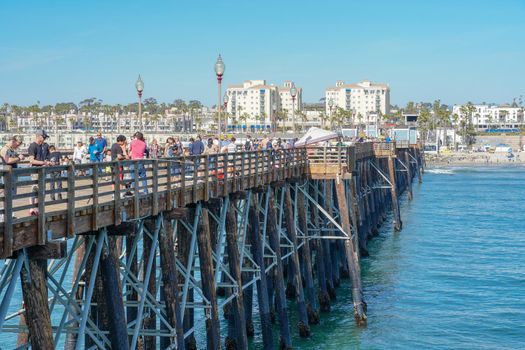 Tourist walking on the Oceanside Pier during blue summer day, Oceanside, northern San Diego, California. Wooden pier on the western United States coastline. Famous for fisher. Febraury 22n, 2020