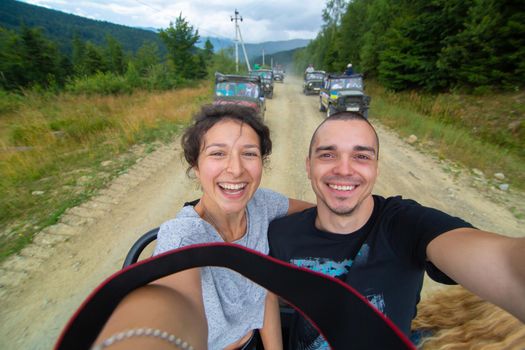 Happy couple take selfie standing on car durring mountain car tour.