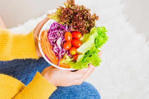 Young woman eating fresh salad meal vegetarian spinach in a bowl, top view of female hands holding bowl with green lettuce salad on legs, Clean detox healthy food concept