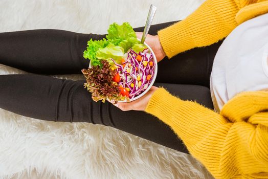 Young woman eating fresh salad meal vegetarian spinach in a bowl, top view of female hands holding bowl with green lettuce salad on legs, Clean detox healthy food concept
