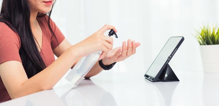 Asian Business young woman working from home office he quarantines disease coronavirus or COVID-19 her cleaning hands with sanitizer gel on front tablet computer