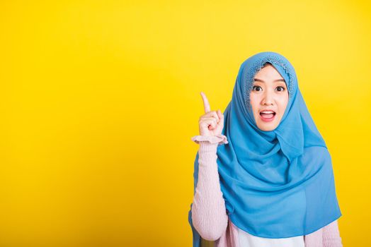 Asian Muslim Arab, Portrait of happy beautiful young woman Islam religious wear veil hijab funny smile she positive expression pointing with finger up to space isolated yellow background