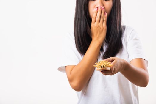 Asian woman unhappy weak hair problem her hold hairbrush with damaged long loss hair in the comb brush on hand and she shocked use hand cover mouth, isolated on white background, Medicine health care