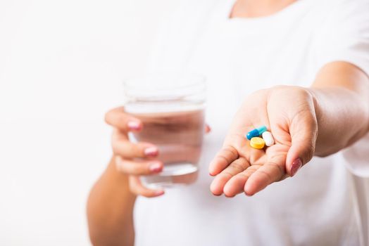 Closeup young Asian woman hold pill drugs in hand ready take medicines with a glass of water, studio shot isolated on white background, Healthcare and medical pharmacy concept