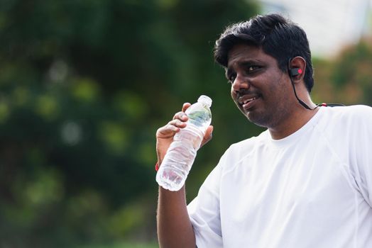 Close up Asian young sport runner black man wear athlete headphones he drinking water from a bottle after running at the outdoor street health park, healthy exercise workout concept