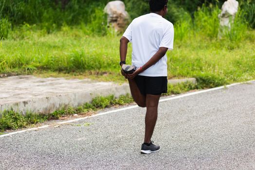 Close up Asian young athlete sport runner black man wear watch lift feet stretching legs and knee before running at the outdoor street health park, healthy exercise before workout concept