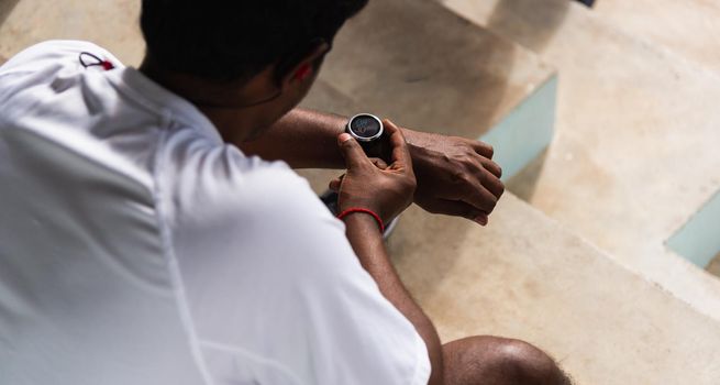 Close up Asian young athlete sport runner black man wear modern time smart watch he sitting resting before training running at the outdoor street health park, healthy exercise before workout concept