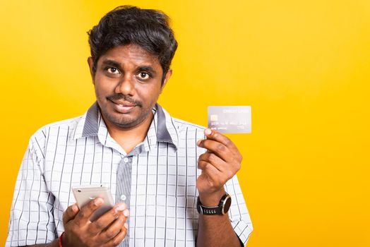 Closeup Asian happy portrait young black man holds a mobile smartphone and showing credit card for mobile payment shopping online concept, studio isolated on yellow background