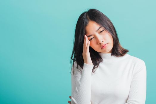 Young beautiful Asian woman holding her hands to her temples with a severe headache, Portrait sad female unhappy suffering from migraine, studio shot isolated on a blue background