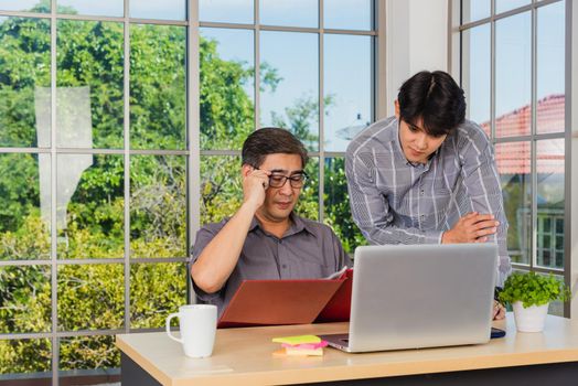 Asian senior and junior two businessmen discuss something during their meeting consultation project, Mature boss with a business partner working together on the laptop computer on desk home office