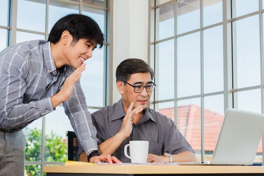 Asian senior and young business man working online on a modern laptop computer he looking the screen meeting online. Old and junior businessman using video call conference on desk table at office