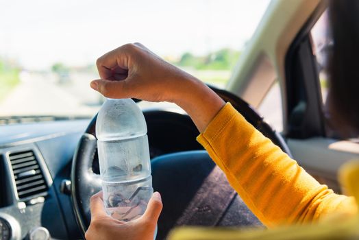 Asian woman holding a water bottle for drink while driving the car in the morning during going to work on highway road, Transportation and vehicle concept