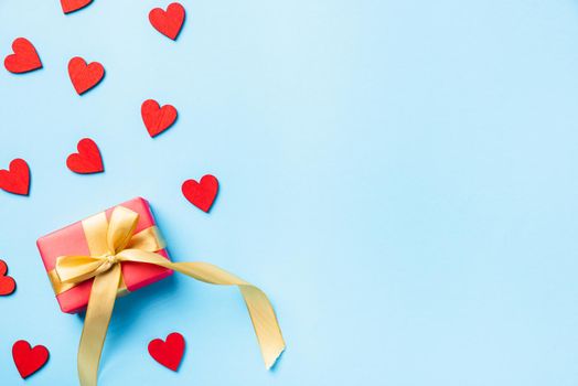 Happy Valentines' day background concept. Red gift box with a golden bow ribbon and wood red hearts composition greeting card for love isolated on blue background with copy space. Top View from above