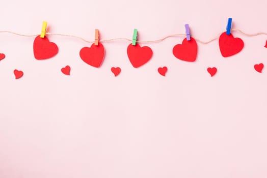 Happy Valentine's day background. red heart shaped valentines decoration hanging with paper clips on the rope for love composition greeting card isolated on pink background with copy space