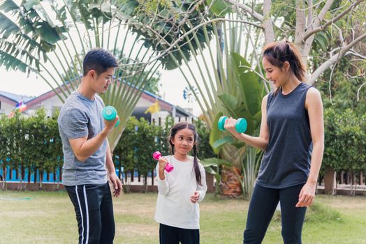 Asian young mother, father and child daughter doing exercising together with dumbbells is fun outdoors in nature a field garden park. Happy family kid sport and exercises for healthy lifestyle