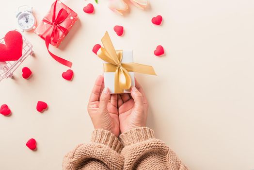 Valentine's day and birthday. Woman hands holding gift or present box decorated and red heart surprise on cream pastel background, Female's hand hold gift box package in craft paper Top view flat lay