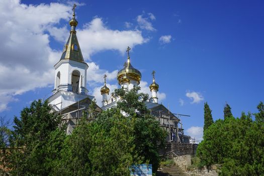 Koktebel, Crimea. The structure of the Christian Church with Golden cupolas surrounded by trees and vegetation.