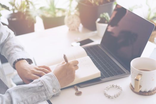 Woman is writing in planner notebook while using laptop to work or plan with workspace at home. Education business lifestyle concept.