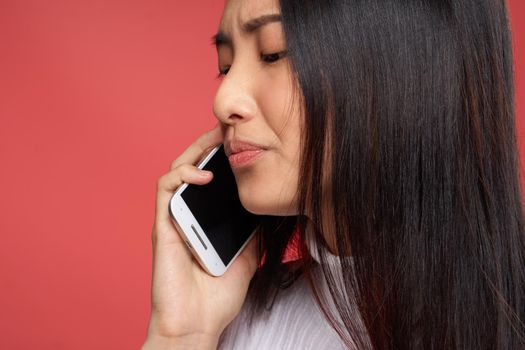 woman of asian appearance and contented facial expression talking on the phone close-up red fund. High quality photo