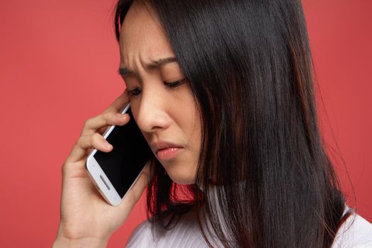 woman of asian appearance and contented facial expression talking on the phone close-up red fund. High quality photo