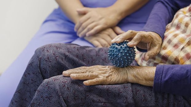 Elderly woman doing rubber ball for exercise fingers, palm ,hand and foot muscle with caregiver take care.