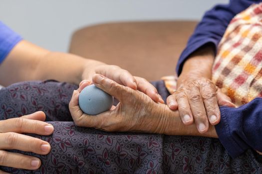 Elderly woman doing rubber ball for exercise fingers, palm ,hand and foot muscle with caregiver take care.