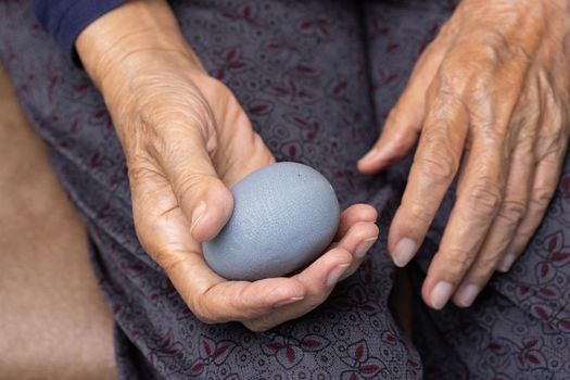 Elderly woman doing rubber ball for exercise fingers, palm ,hand and foot muscle with caregiver take care.