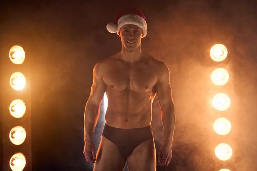 Portrait of muscular man wearing Christmas Santa hat, standing athletic pose on smoky background Macho Shirtless Naked torso stripper Hot sexy Santa guy Seductive male for holiday