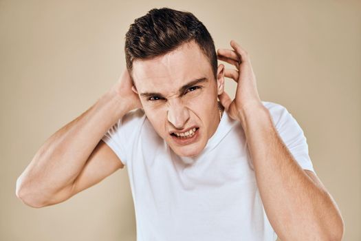 Man with displeased facial expression emotions white t-shirt gestures with hands beige background. High quality photo