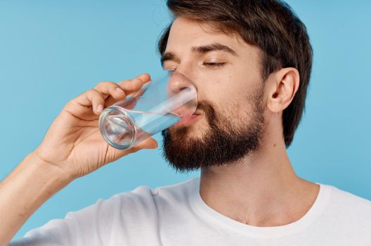beautiful man drinking water from a glass on a blue background close-up portrait. High quality photo