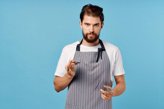 a man hairdresser in a gray apron does his hair on a blue background scissors comb. High quality photo